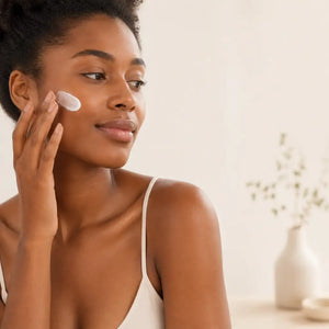A woman applying a white, creamy moisturizer to her cheek with her fingertips.